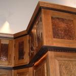 Upper cabinets with accent lighting show off texture of gouged panels and hammered copper panel cabinet doors above.